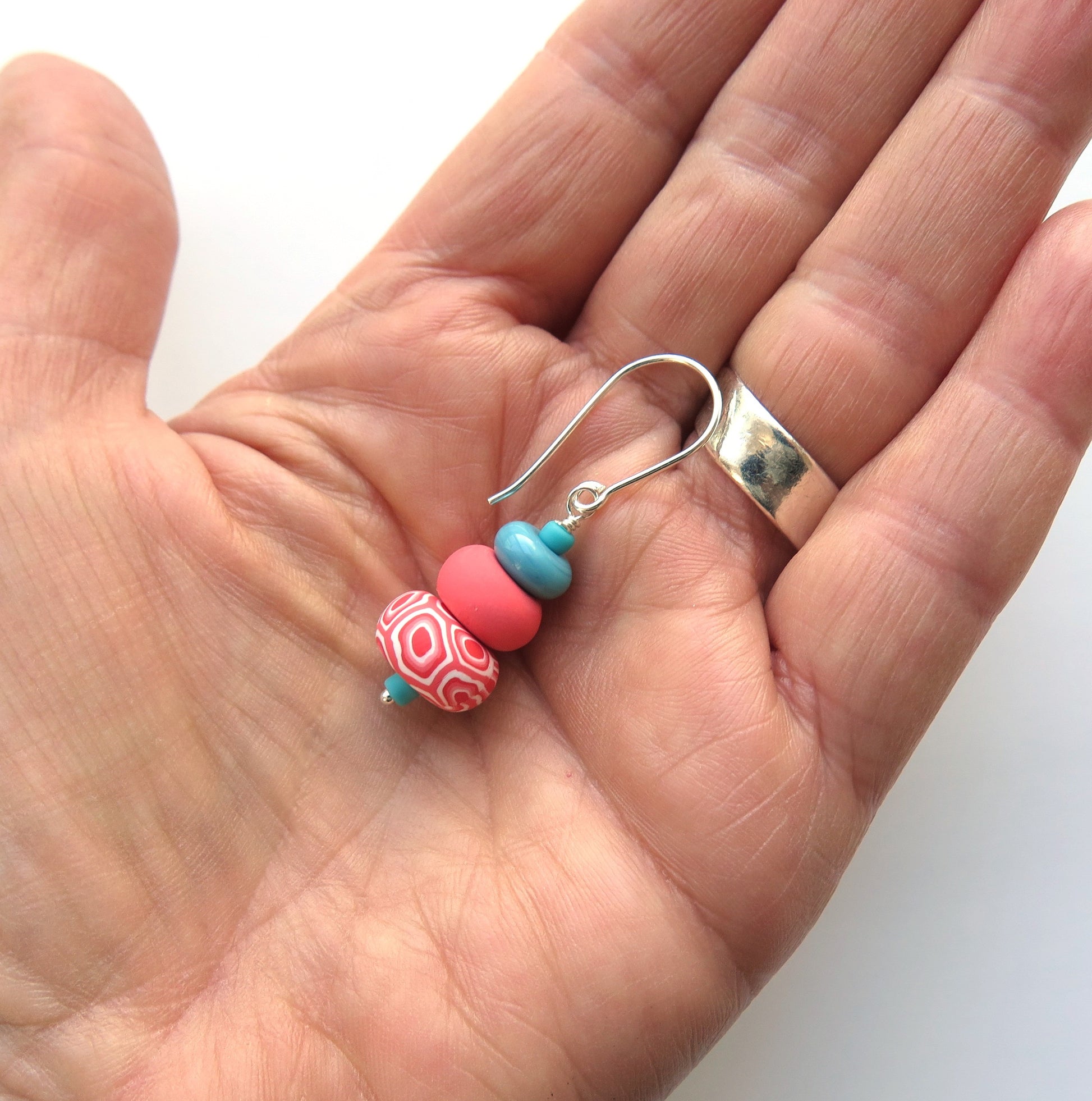 Hand holding a silver earring with colorful beads against a white background